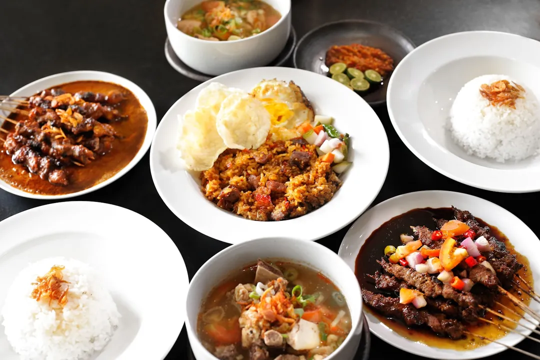 Sate, nasi goreng, sop buntut dan nasi putih di atas meja gelap